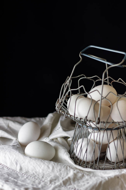 Old metal egg cup containing white eggs, on white tablecloth and black background. Chicken egg. Copy, empty space for text. - Fotoğraf, Görsel