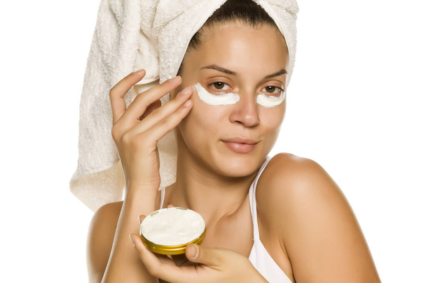 junge Frau trägt Gesichtscreme unter ihren Augen auf weißem Hintergrund auf - Foto, Bild