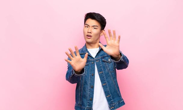 young chinese man feeling terrified, backing off and screaming in horror and panic, reacting to a nightmare against flat color wall - Foto, Bild
