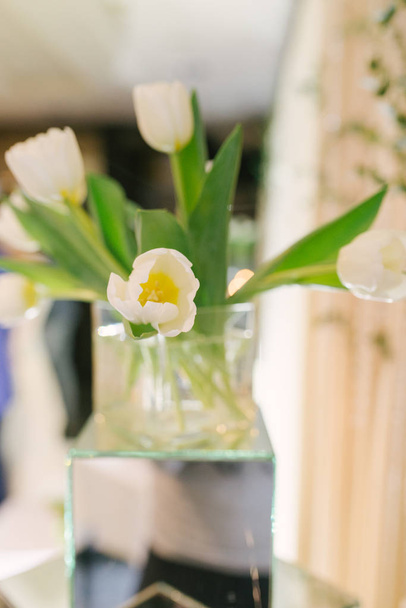 Bouquet of white tulips in a glass vase in the interior decor or wedding. Selective focus - Foto, afbeelding