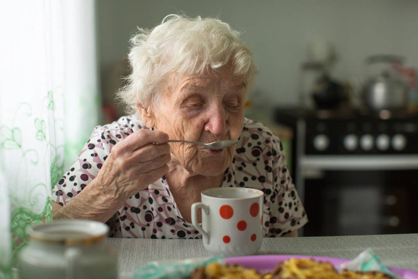 Vanha nainen istuu keittiössä ja juo teetä.
.  - Valokuva, kuva