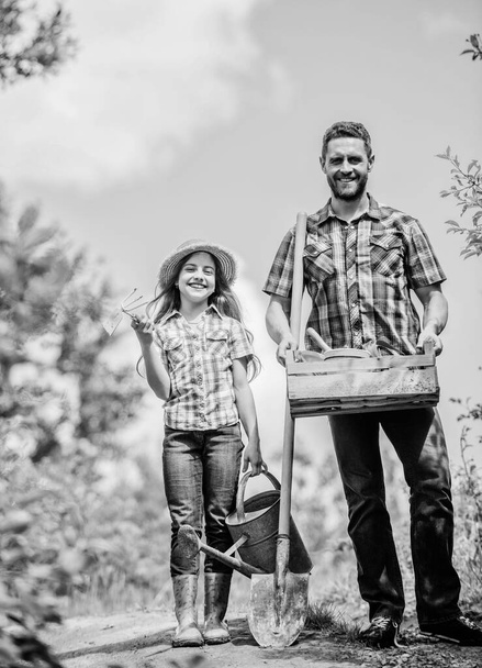father and daughter on rancho. summer farming. farmer man with little girl. garden tools, shovel and watering can. kid worker with dad. family bonding. spring country side village. Flower watering - Foto, immagini