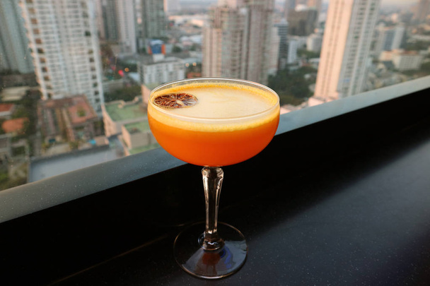 vibrierender orangefarbener Cocktail auf der Dachterrasse mit Stadtblick aus der Luft im Hintergrund - Foto, Bild