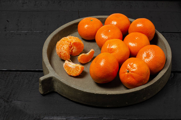 Mandarin oranges on concrete dish on black background - Photo, image