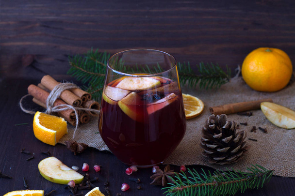 Glass of red wine with spices. Glass of red hot mulled wine in the centre with apple and spices with sticks cinnamon on a wooden table with slices of orange. horizontal. Winter and autumn hot drinks. - Photo, Image