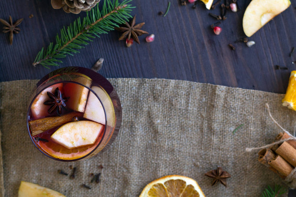 Kerststilleven. Warme winter- en herfstdranken. Glas rode warme glühwein met appel en specerijen met stokjes kaneel op een houten tafel met schijfjes sinaasappel en jute. Bovenaanzicht. kopieerruimte - Foto, afbeelding