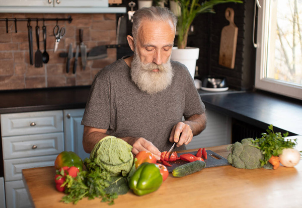 Bearded senior Man preparing healthy and tasty salad in kitchen. - Fotografie, Obrázek