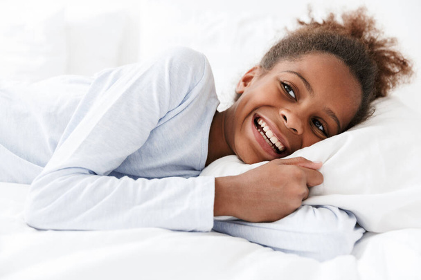 Image of african american little girl smiling and lying in bed a - Фото, зображення