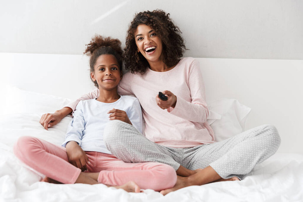 Image of african american woman and her daughter watching tv on  - Fotoğraf, Görsel