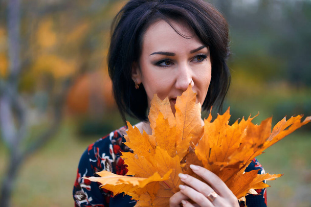 Hermosa mujer elegante de pie y posando con ramo de hojas amarillas en el parque de la ciudad de otoño, cara de primer plano
 - Foto, Imagen