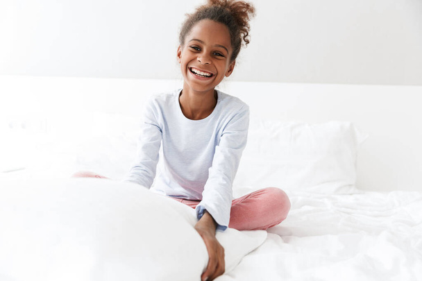 Image of african american little girl smiling and sitting in bed - Foto, Imagen