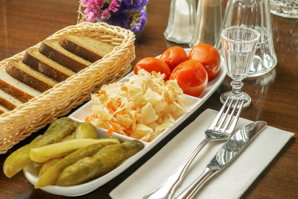 Белая большая тарелка с консервированными помидорами, капустой и огурцами
 - Фото, изображение