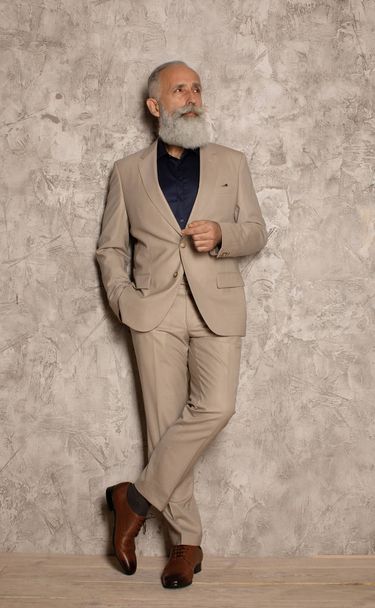 Confident bearded mature businessman wearing suit standing isolated over grey background. - Zdjęcie, obraz