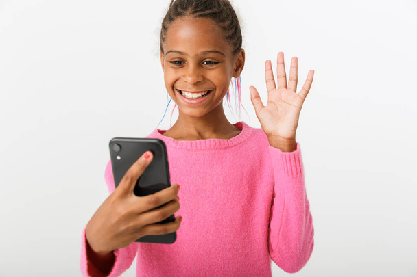 Image of pretty african american girl holding cellphone and waving hand - Fotó, kép