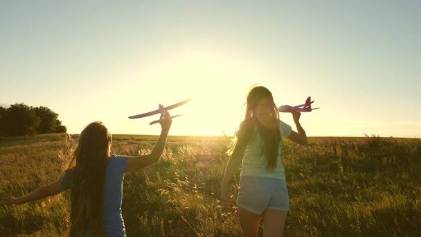 Marzenie o lataniu. Szczęśliwego dzieciństwa. Dwie dziewczyny bawią się zabawkowym samolotem o zachodzie słońca. Dzieci na tle słońca z samolotem w ręku. Sylwetka dzieci bawiących się w samolocie - Zdjęcie, obraz