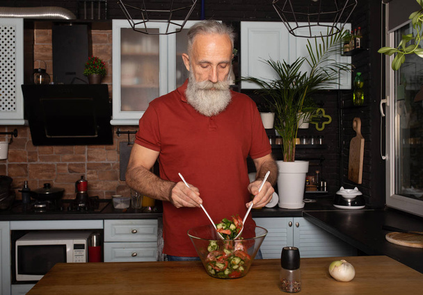 Bearded senior Man preparing healthy and tasty salad in kitchen. - Foto, Bild