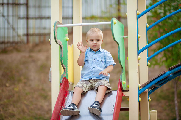 La vita quotidiana di un bambino con disabilità. Un ragazzo con la sindrome di Down sta giocando nel parco giochi. Disturbo cromosomico e genetico nel bambino
. - Foto, immagini