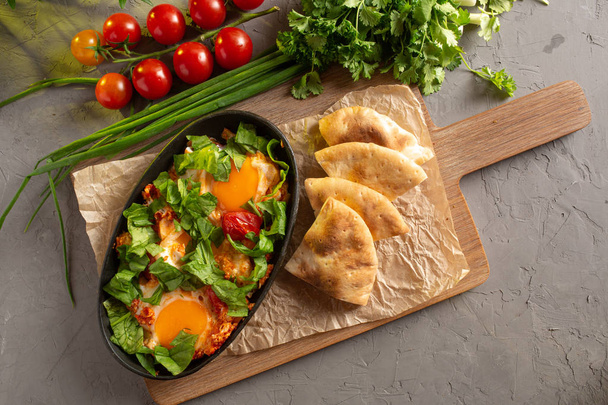 fried eggs with tomatoes and herbs in an oval black dish - Foto, imagen