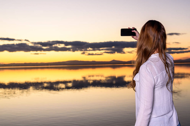 Молода дівчина на заході сонця бере селфі зі своїм смартфоном, візіті
 - Фото, зображення