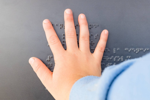Το χέρι ενός τυφλού παιδιού σε ένα κείμενο γραμμένο σε γραφή Μπράιγ. - Φωτογραφία, εικόνα