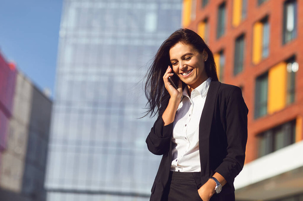 Hispanic businesswoman smiling speaks on a mobile outdoors - 写真・画像