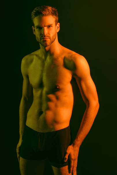 色の光と黒の隔離されたフォントの背景に黒の下着で強い裸の筋肉男性モデル - 写真・画像