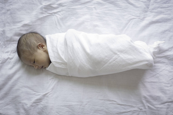 Beyaz yatağa kumaş sarılı yeni doğmuş bebek. - Fotoğraf, Görsel