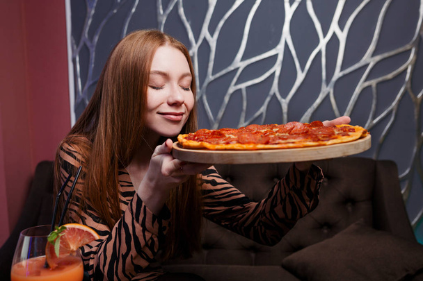 Red-haired girl holds a pizza in her hands and inhales its aroma - Valokuva, kuva