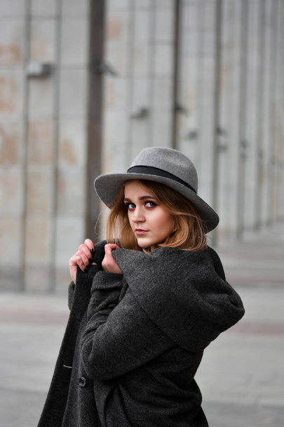 Portrait of beautiful woman wearing hat and gray coat. Outdoor portrait in city - Фото, зображення