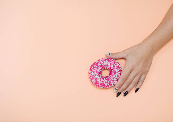 Eetlust donuts met glazuur op een gekleurde achtergrond met vrouwelijke handen met een mooie manicure. - Foto, afbeelding