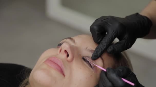 Professional beautician in a beauty salon straightens eyelashes to a client. - Footage, Video
