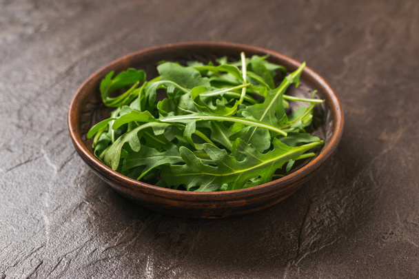 Clay bowl with fresh arugula on a dark stone background. Healthy plant-based diet. - Photo, Image