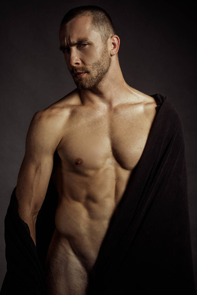 Modelo masculino muscular despojado fuerte en tela negra sobre fondo de fuente aislado negro
 - Foto, Imagen