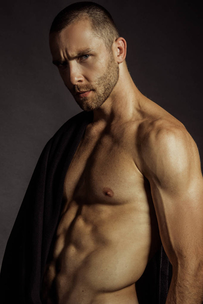 Strong stripped muscle male model in black fabric on black isolated font background - Fotografie, Obrázek