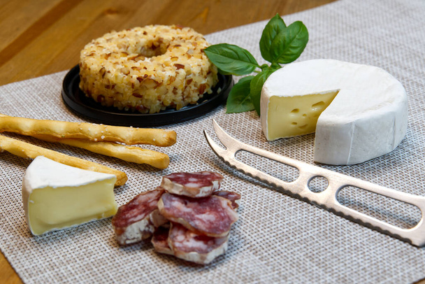 Sajt előétel választás vagy sajt és bor party asztal. Brie sajt, kenyér pálcika és szalámi nagy előétel tostart a vacsora. - Fotó, kép