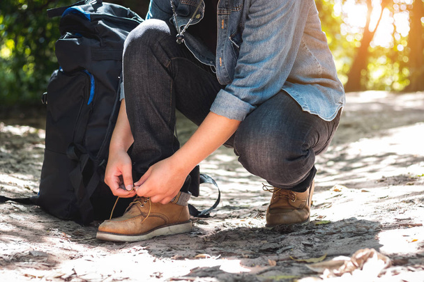 男は森の中でハイキングの準備をしながら靴ひもを結んでいる. - 写真・画像