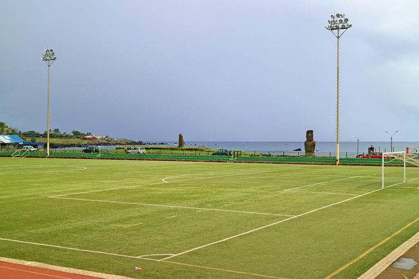 Football Field at Hanga Roa Town with Ahu Tautira sanctuary and Pacific Ocean in the Backdrop, Easter Island, Chile - 写真・画像