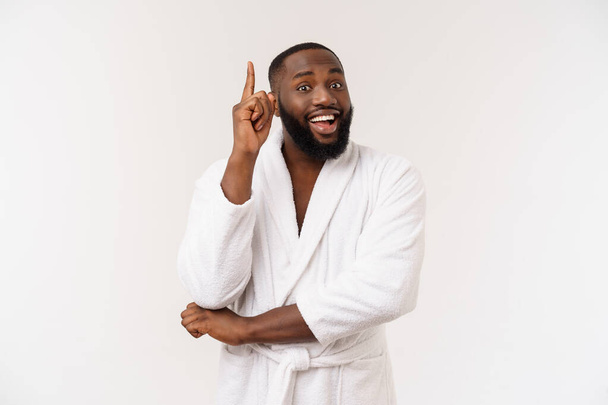 Zwarte kerel het dragen van een badjas wijzend vinger met verrassing en gelukkige emotie. Geïsoleerde over whtie achtergrond. - Foto, afbeelding