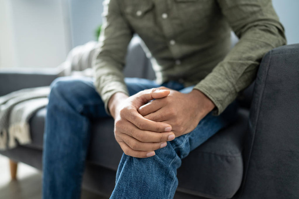 Man Suffering From Knee Pain Sitting On Sofa - Foto, afbeelding
