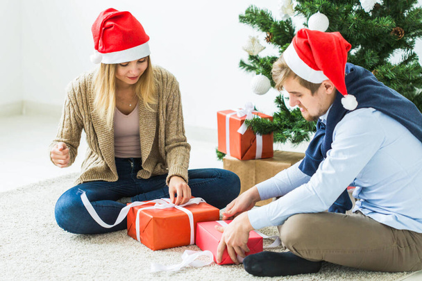 έννοια των διακοπών - Γλυκό ζευγάρι άνοιγμα χριστουγεννιάτικα δώρα, κάθεται στο σαλόνι - Φωτογραφία, εικόνα