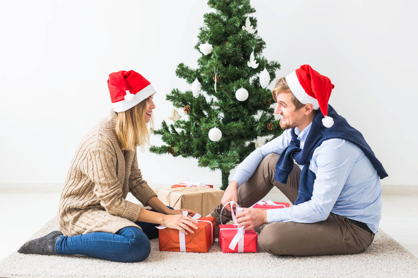 Concepto de vacaciones - Dulce pareja abriendo regalos de Navidad, sentado en la sala de estar
 - Foto, Imagen