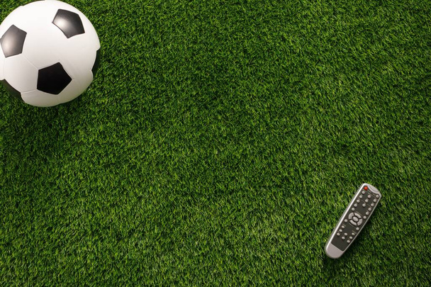 Soccer ball on a green field and a TV remote control. Flat lay c - Foto, Imagen