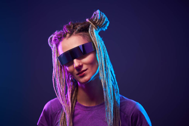 Улыбающаяся девушка в солнечных очках смотрит на камеру в неоновом свете
 - Фото, изображение