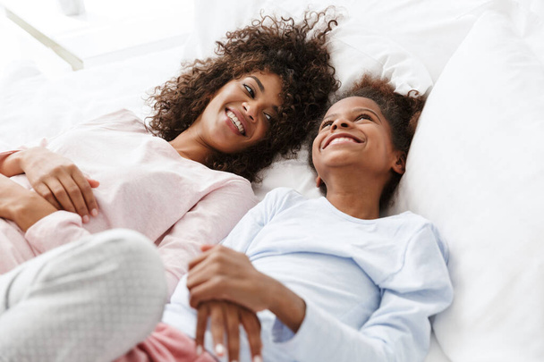 Image of cheerful african american woman and her daughter lying  - Fotó, kép