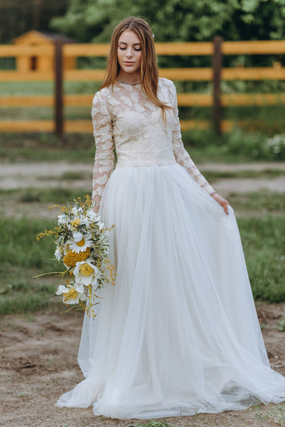 A beautiful young bride with a bouquet of daisies in a field - Foto, Imagen