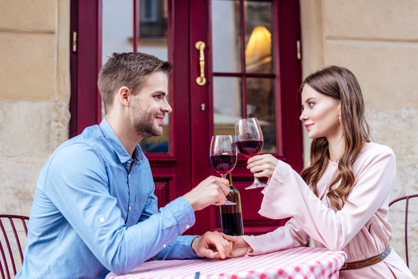 heureux, couple élégant assis dans la rue café et verres cliquetis de vin rouge
 - Photo, image