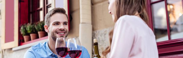 plano panorámico de pareja joven sentada en la cafetería de la calle con copas de vino tinto
 - Foto, imagen