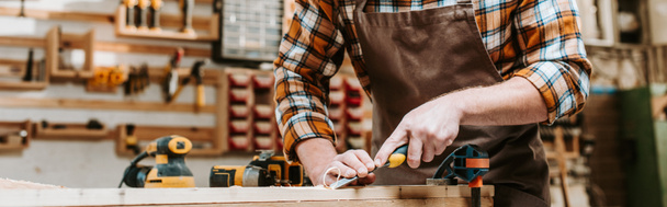 plano panorámico de carpintero sosteniendo cincel mientras tallaba madera en taller
  - Foto, Imagen