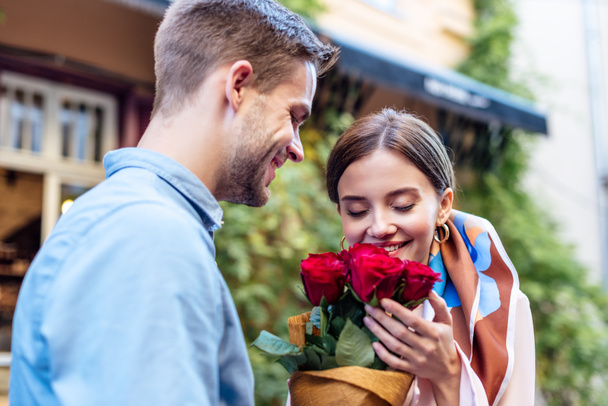 smiling man presenting bouquet of roses to happy girlfriend on street - Fotó, kép