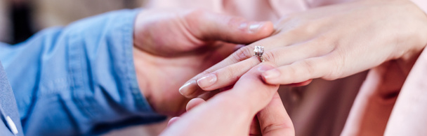 vista recortada del hombre poniendo anillo de bodas en el dedo de la novia, tiro panorámico
 - Foto, imagen